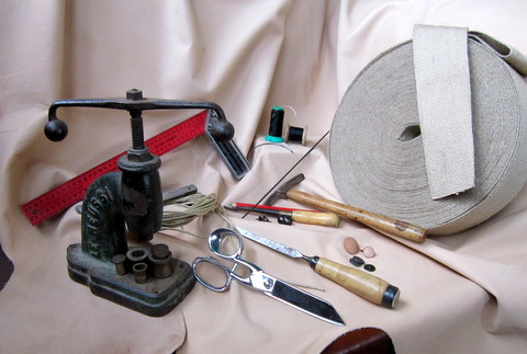 Some of our tools used to renovate old leather furniture in our leather workshop in Brittany, l'Atelier du cuir - Bretagne. The button machine, scissors, hammer and so forth lie on raw leather. The raw leather is colored and given a patina during the renovation process in order to replace the ancient leather when needed.