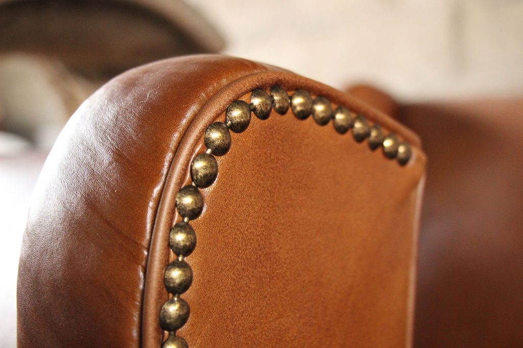 Detail of the armrest of a entirely renovated leather armchair. The leather is new and given the patina of the ancient leather color in our leather workshop in Brittany, l'Atelier du cuir - Bretagne. It is decorated with a band of brass nails.